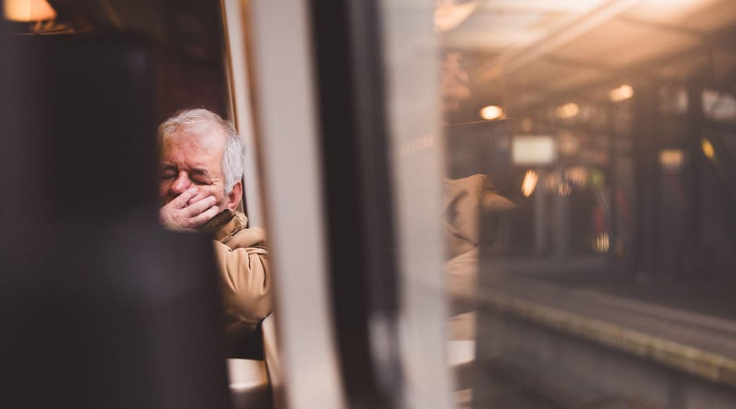 Older man sat on a train struggling with how to deal with fatigue